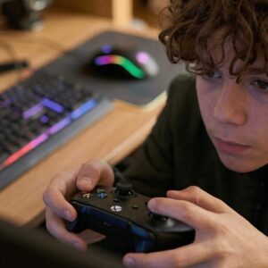 Teen holding a video game controller intent on the game he is playing.